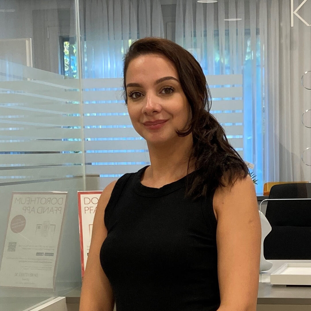 filialleiterin-in-schwarzem-kleid-steht-laechelnd-vor-einem-schalter