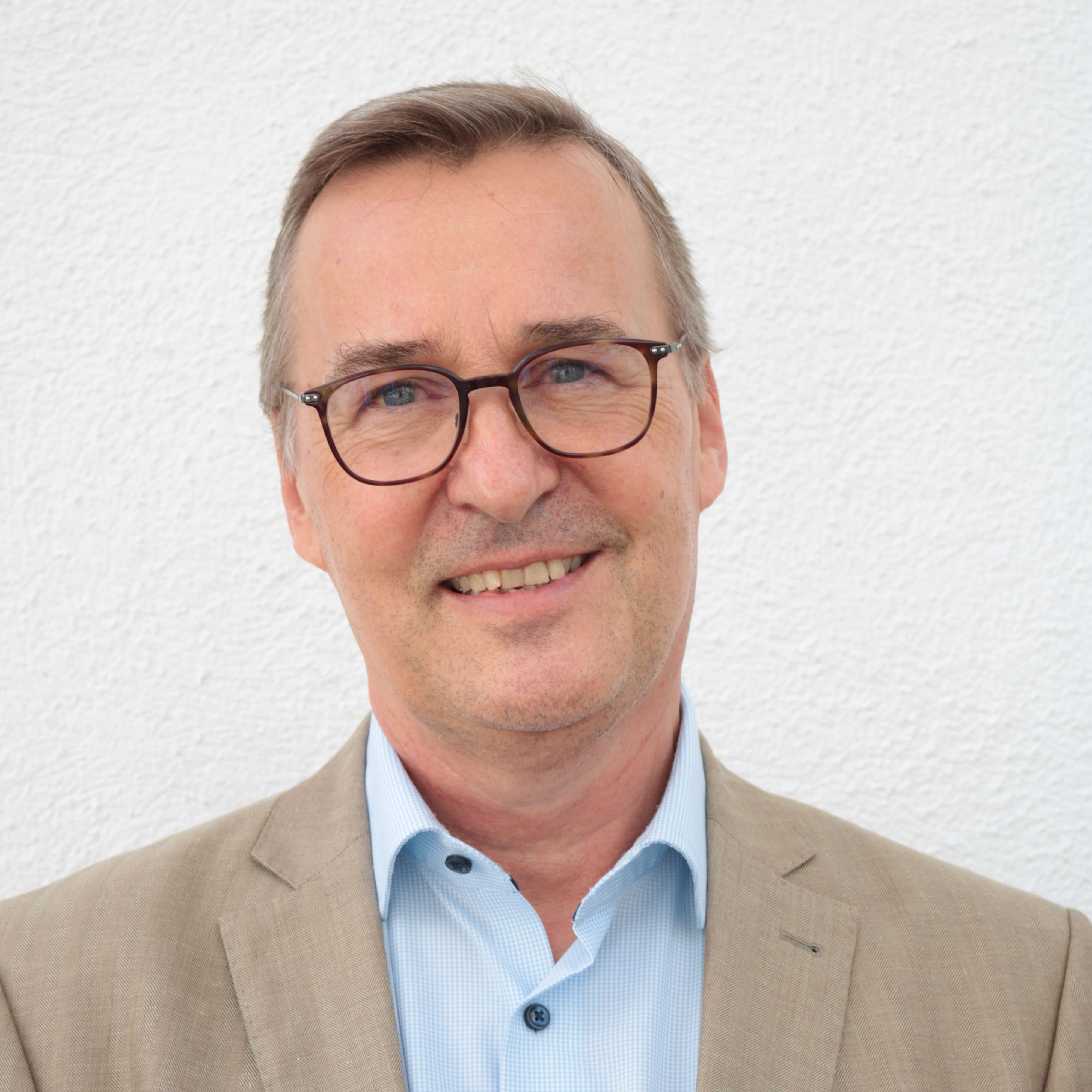 filialleiter-laechelnd-in-einem-braunen-anzug-vor-einer-grauen-wand