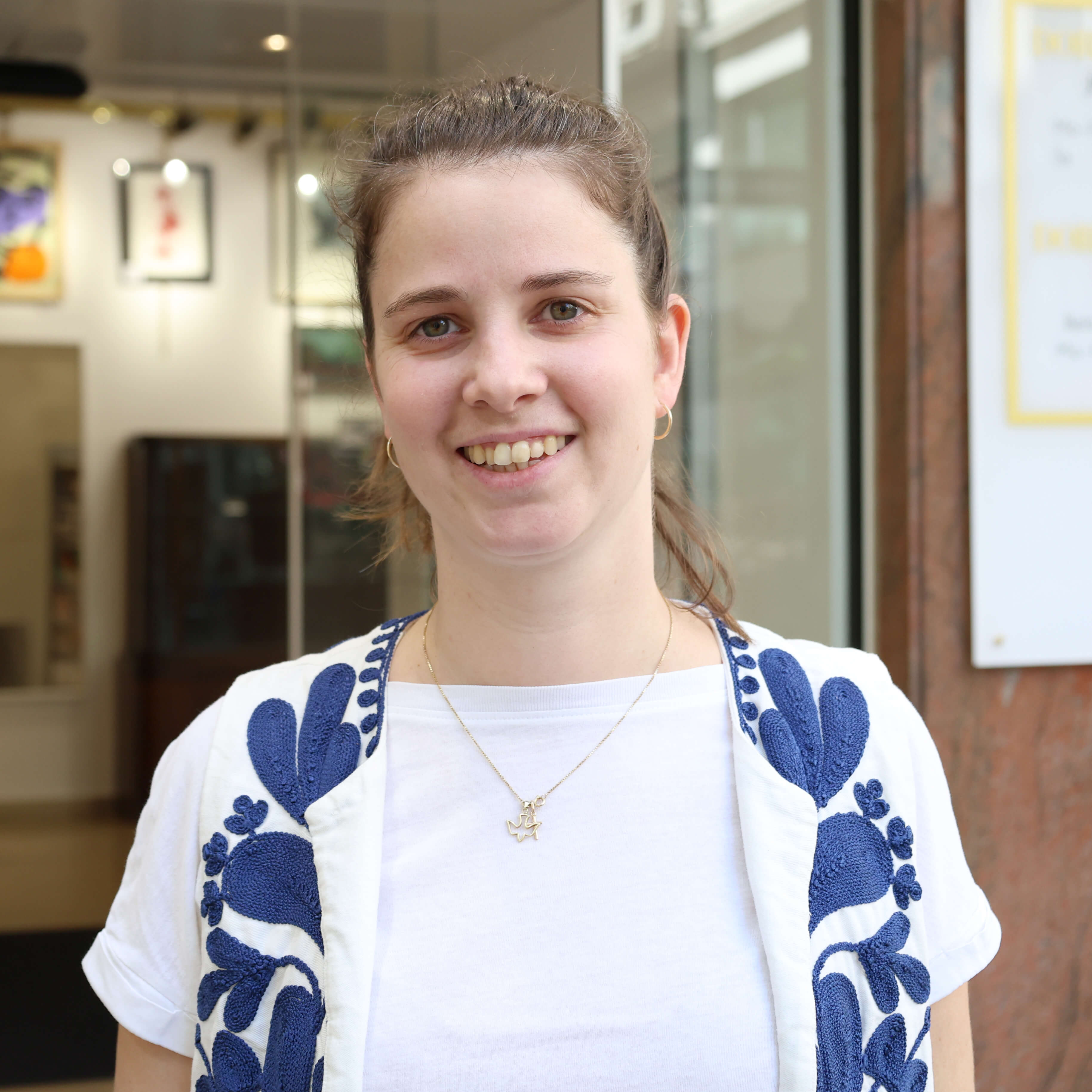 filialleiterin-mit-zopf-und-halskette-steht-vor-gebäude-und-lächelt