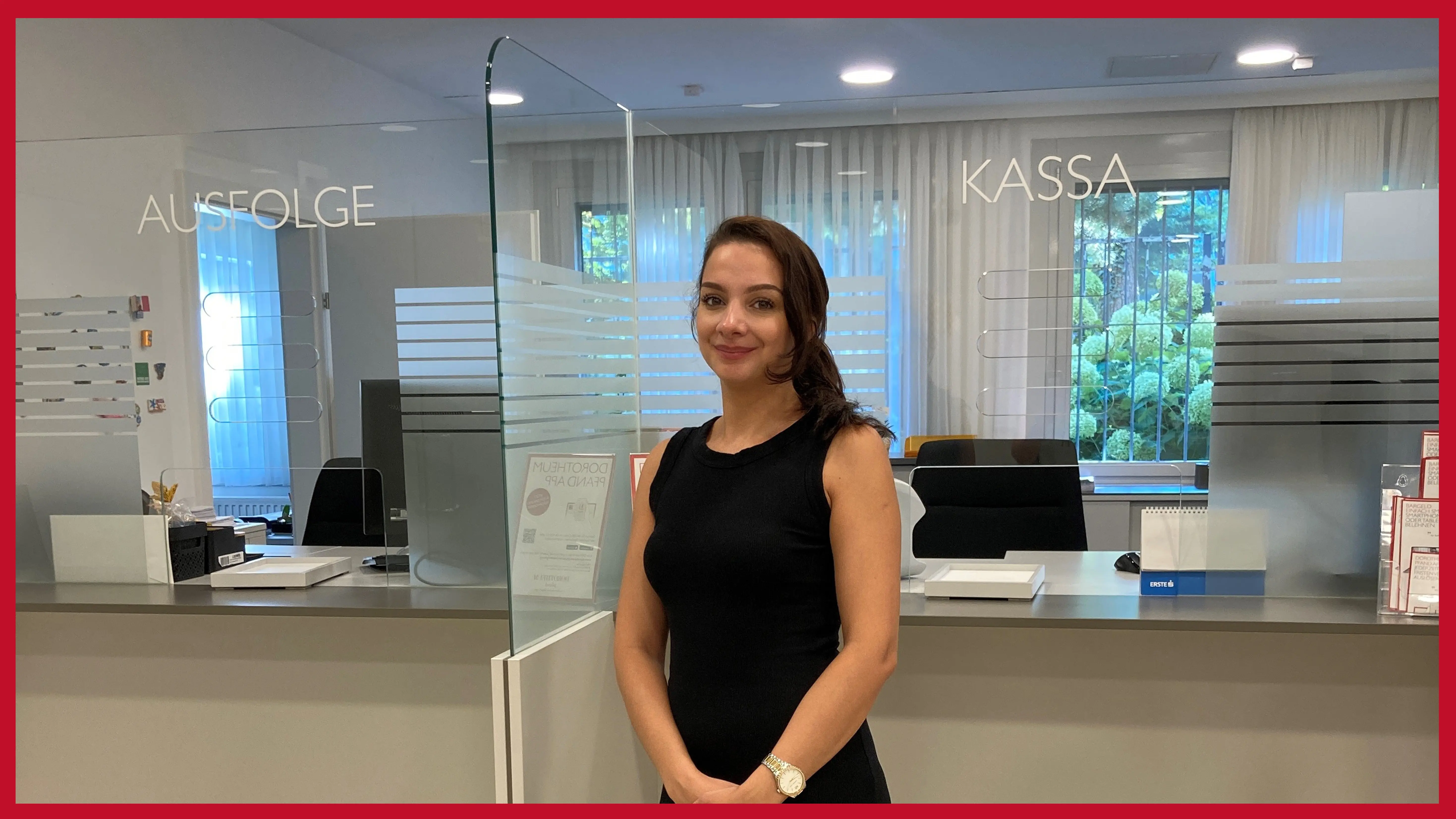 filialleiterin-in-schwarzem-kleid-steht-laechelnd-vor-einem-schalter