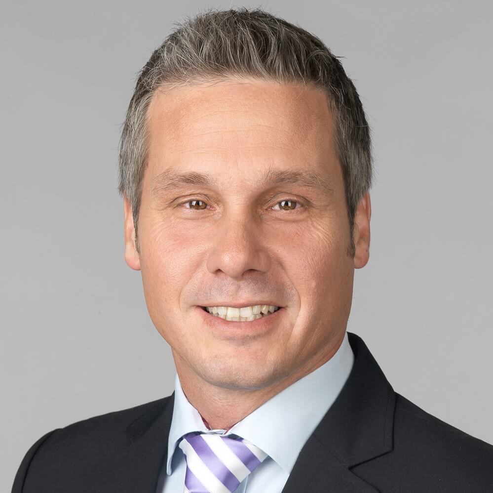 filialleiter-in-anzug-mit-krawatte-laechelnd-vor-grauem-hintergrund