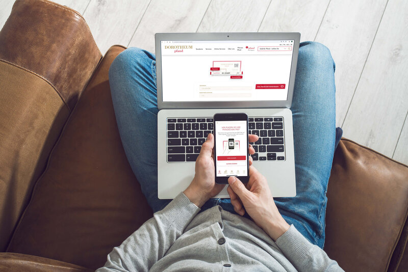 Mann mit Laptop und Smartphone auf der Couch und betrachtet die Dorotheum Pfand Website